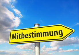 Gelber Wegweiser mit Aufschrift „Mitbestimmung“ vor blauem Himmel mit einigen Wolken