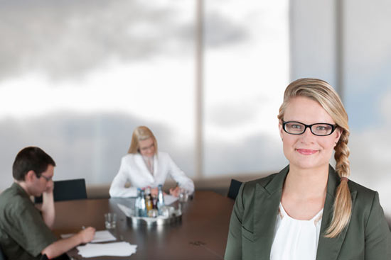 Frau mit Brille vor Konferenztisch, an dem 2 Leute arbeiten