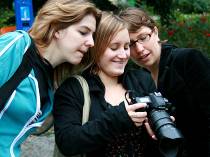 Drei Studentinnen schauen auf den Bildschirm einer professionellen Fotokamera