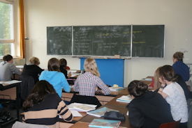 Schulklasse aus Sicht des hinteren Teils des Klassenraumes mit Blick auf die Tafel