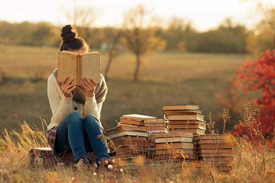 Junge Frau sitzt ein Buch lesend auf einer Wiese