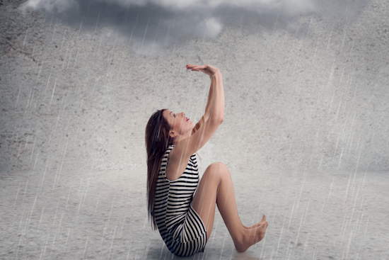 Frau sitzt unter einer Wolke, die regnet.