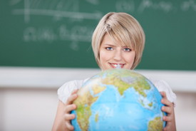 Blonde Frau mit einem Globus in der Hand vor dem Hintergrund einer Tafel