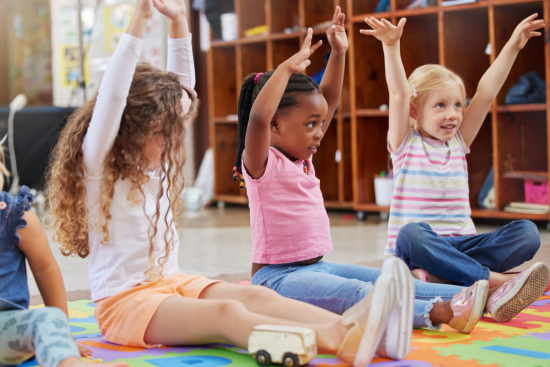 Kinder im Kindergarten sitzen auf dem Boden und heben ihre Hände in die Luft