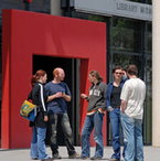 Eine Gruppe Studierender vor einer Bibliothek mit rotem Eingang