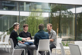 Studierende sitzen draußen an einem Tisch auf dem Campus