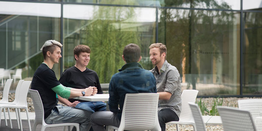 Studierende sitzen draußen an einem Tisch auf dem Campus