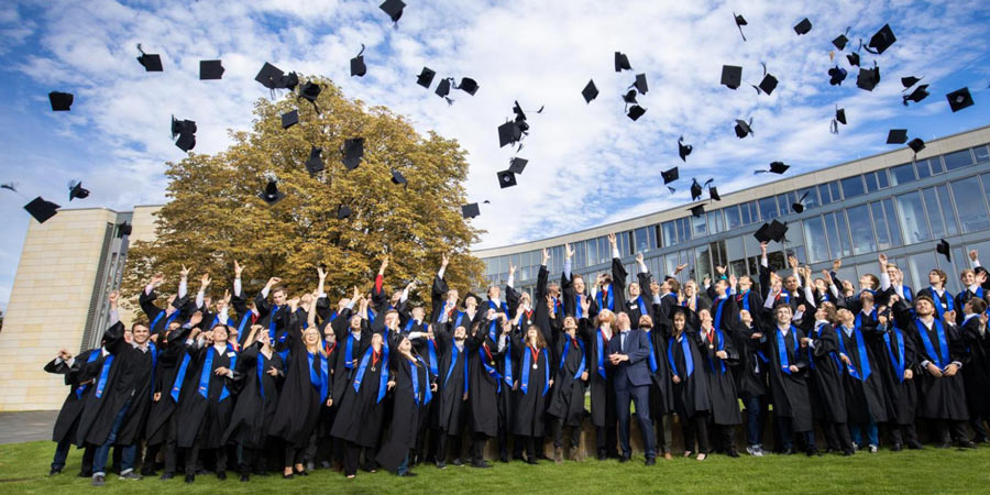 Gruppenbild eines Abschlussjahrgangs: Die Studierenden werfen ihre Hüte in die Luft
