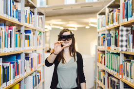 Studierende zwischen Bücherregalen in der Bibliothek mit Virtual Reality-Brille