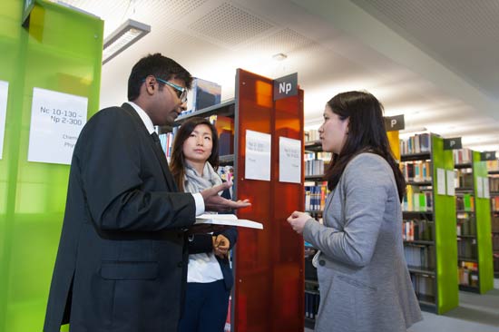 Drei Studierende diskutieren in der Bibliothek