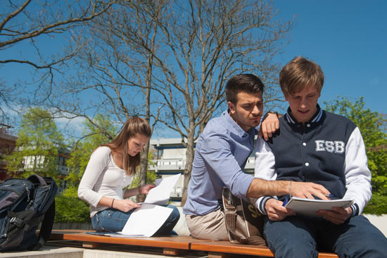 Zwei Studenten und eine Studentin arbeiten draußen mit ihren Unterlagen