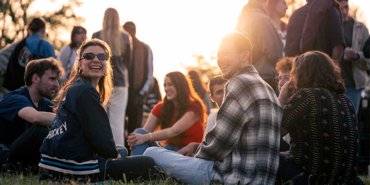 Studierende sitzen lachend auf einer Wiese