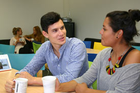 2 Studierende im Gespräch in Cafeteria, im Hintergrund weitere Studierende