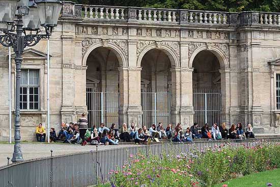 Studierende sitzen unter den Arkaden ihrer Hochschule