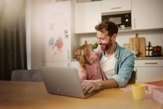 Vater vor Laptop mit Kind auf dem Schoss