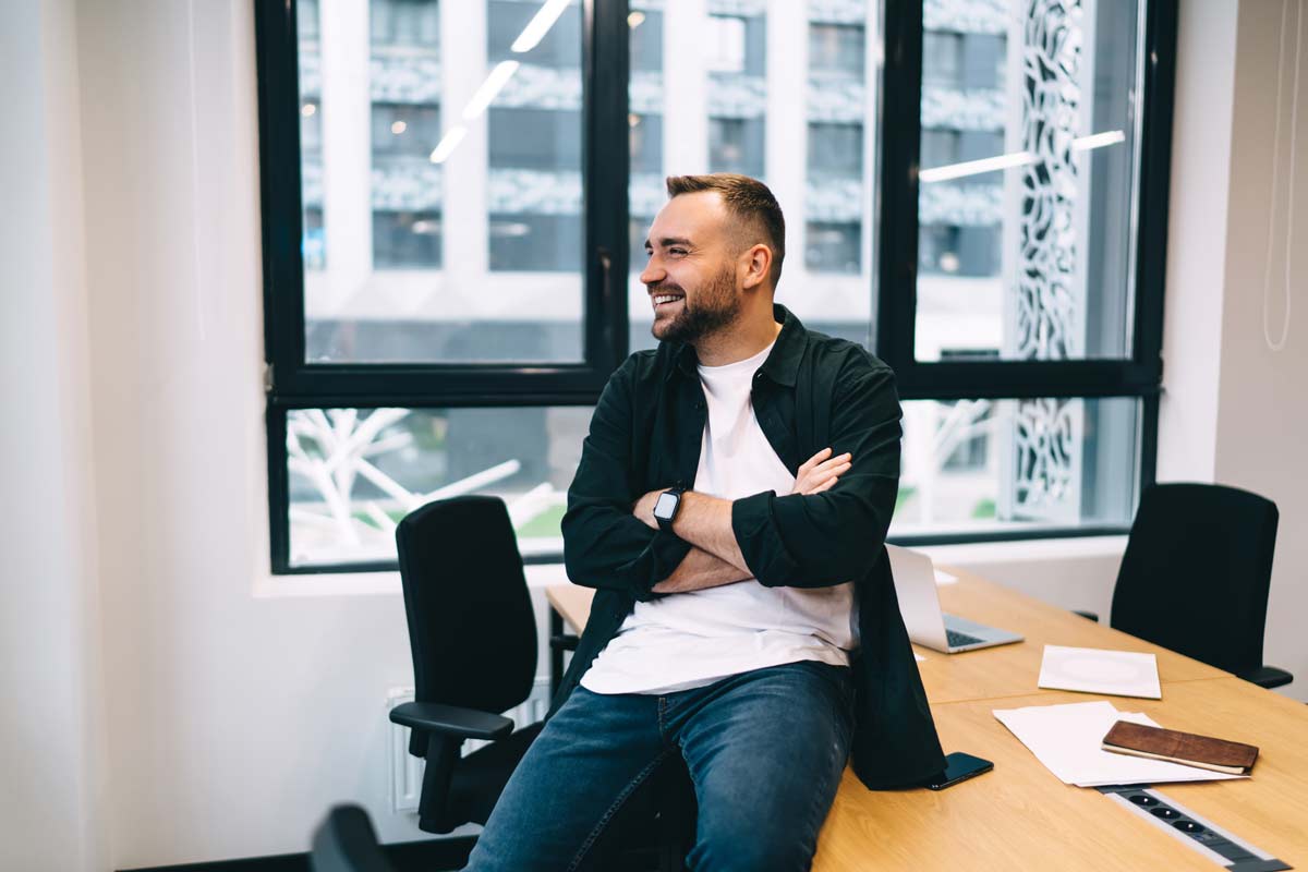 Betriebswirtschaftler lehnt lässig am Schreibtisch