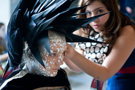 Studierende bereitet Model mit schwarzem stacheligem Kopfschmuck auf Modenschau vor