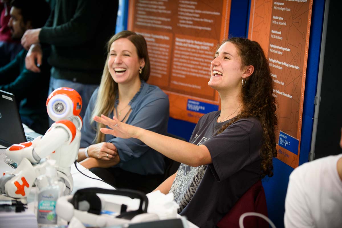Zwei Studentinnen mit Roboter lachen