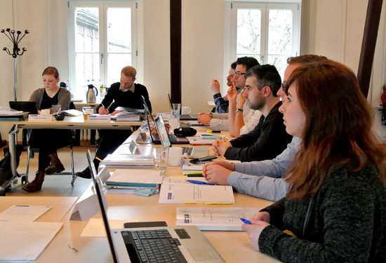 Studierende sitzen mit ihren Laptops an Tischen im Seminarraum