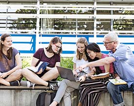 Studierende sitzen und arbeiten draussen zusammen.