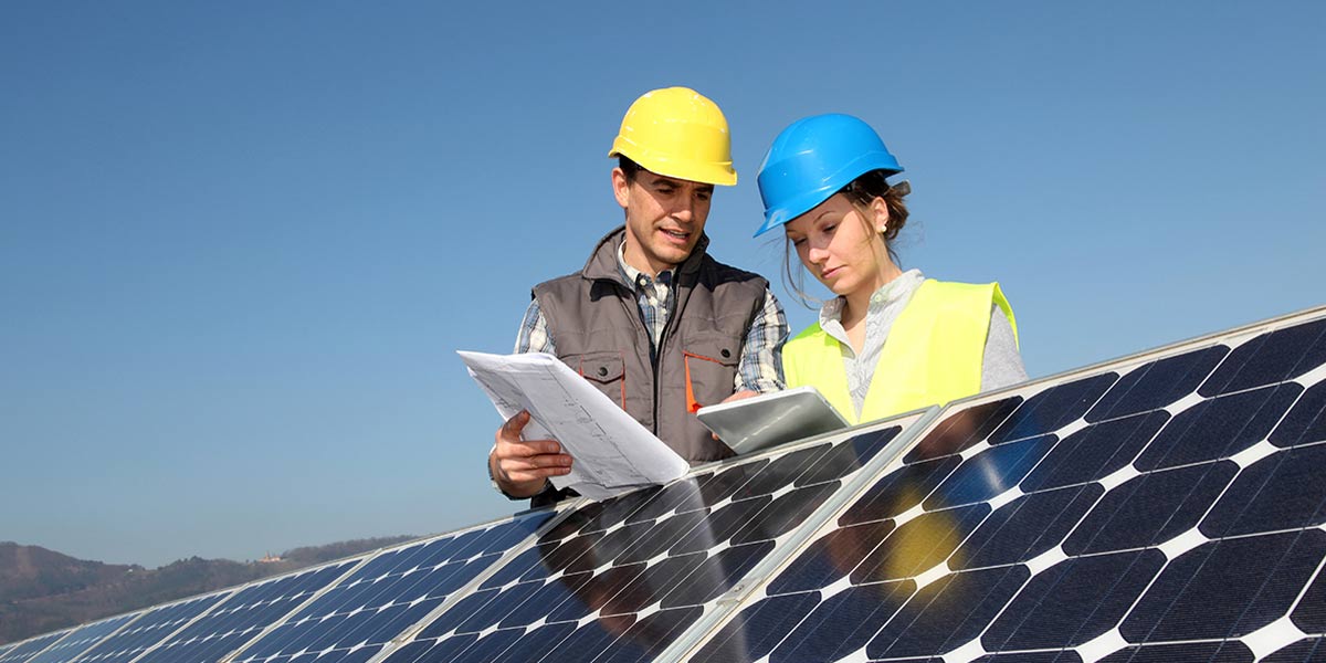 Mann und Frau mit Schutzhelmen stehen draußen vor Solarpanel