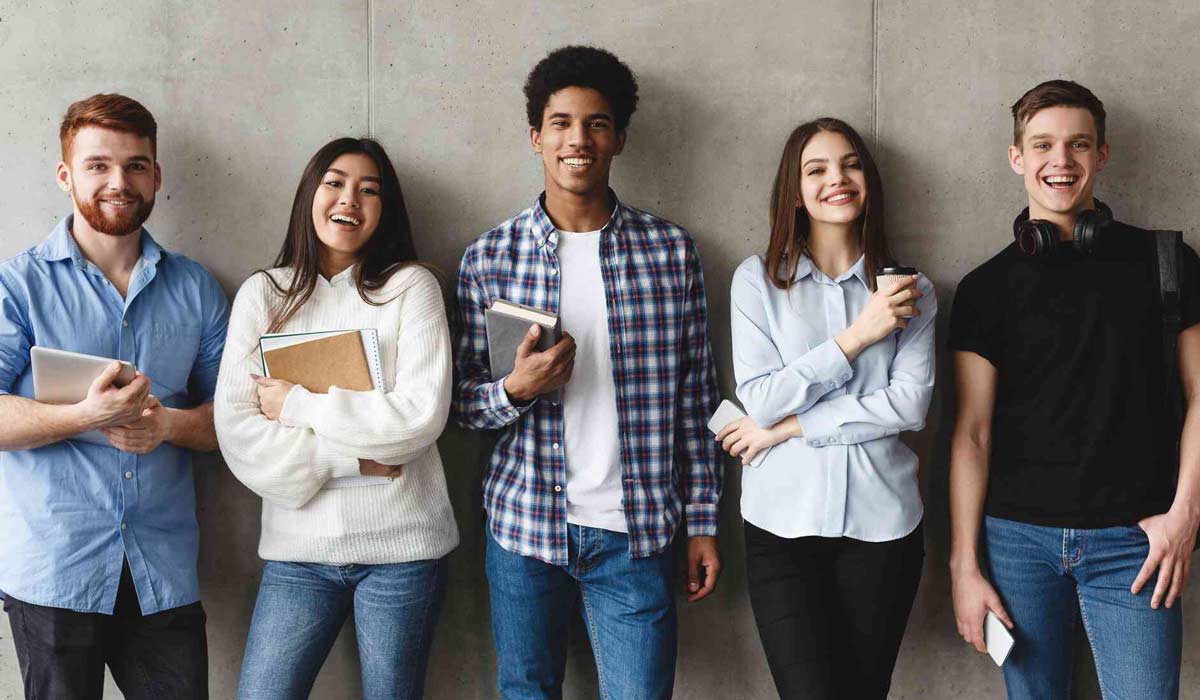 Mehrere Junge Menschen stehen nebeneinander vor einer Wand und schauen in die Kamera