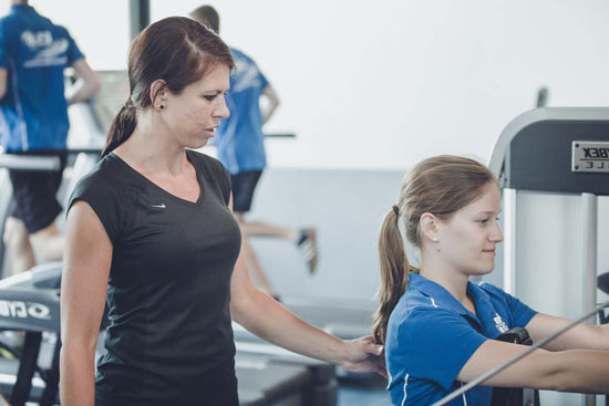 Eine junge Frau steht neben einer anderen, die am Sportgerät ist