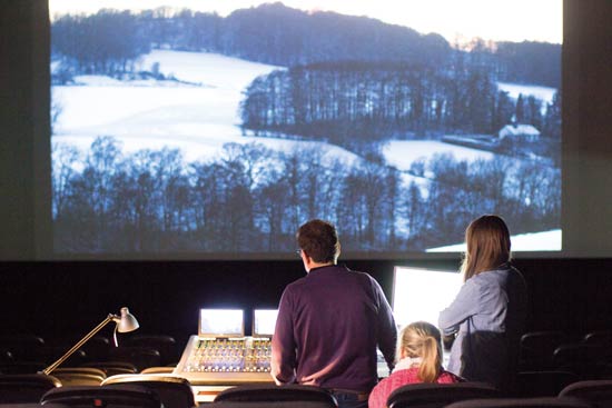 Studierende beim Schneiden des Films. Der Film ist vor ihnen auf großer Leinwand.