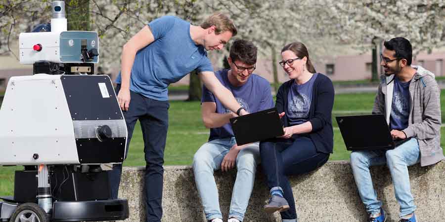 Studis sitzen mit einem Roboter auf dem Campus