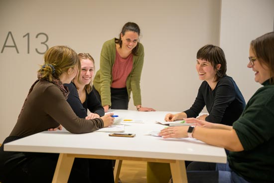 5 Studierende am Tisch, lachend bei der Besprechung/Arbeit