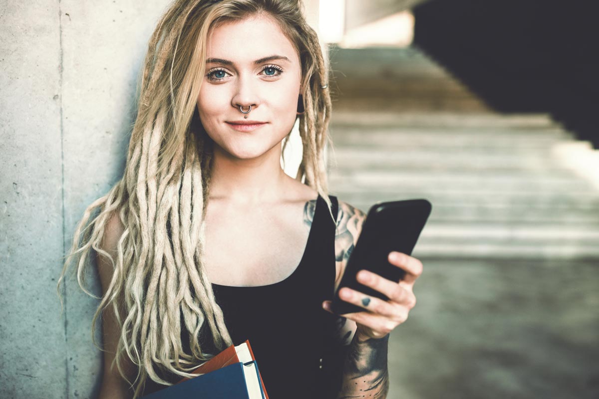 Frau mit Dreads und Smartphone schaut in die Kamera