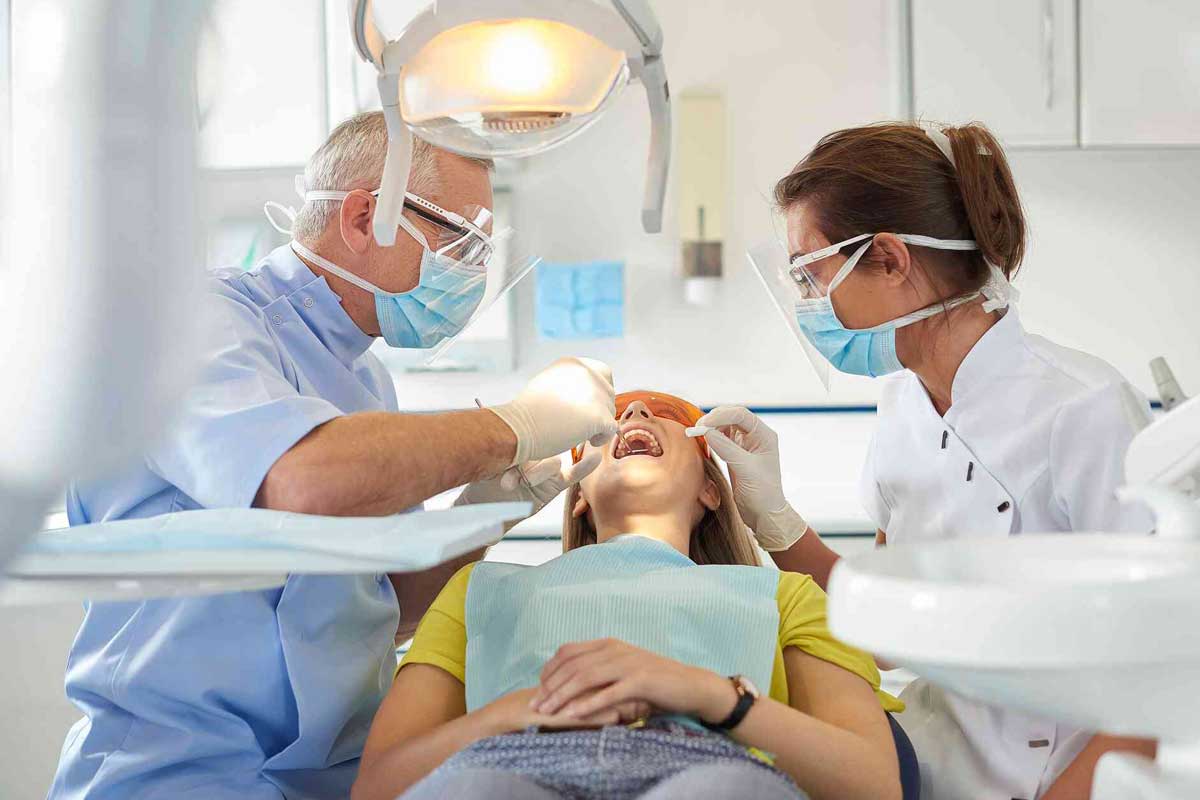 Zwei Zahnmediziner beugen sich über Patientin