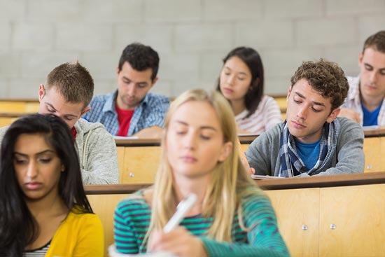 StudentInnen sitzen im Hörsaal und schreiben (eine Klausur)