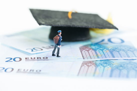 Miniaturfigur steht auf 20 € Scheinen, weiter hinten kleiner Doktorhut
