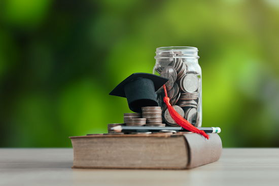 Mini-Doktorhut auf Geldstücken neben einem Glas mit Geldstücken, darunter ein altes Buch. Symbolisch für Studiengebühren.