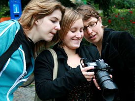 Drei Studentinnen schauen auf den Bildschirm einer professionellen Fotokamera