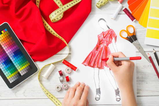Skizze eines Kleides, umgeben von Stoffschere, Maßband, Farbpalette auf Smartphone