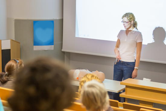 Bildrecht: kasto - stock.adobe.com Frau spricht vor Publikum in Hörsaal - vor ihr liegt ein Dummy mit Defibrilator