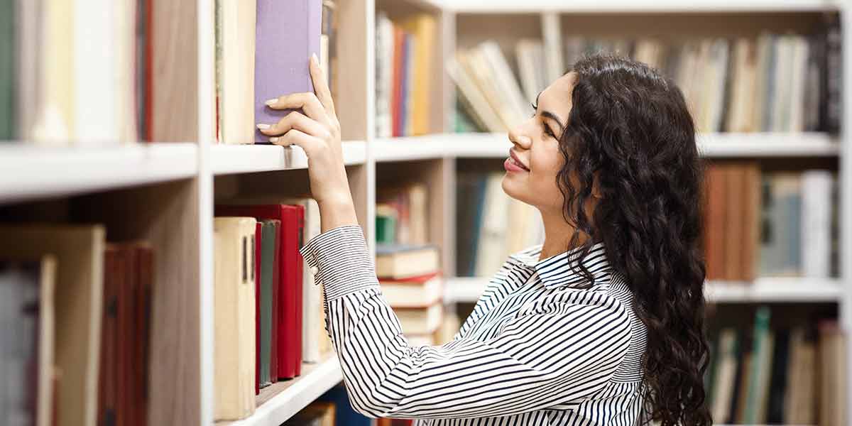 Eine junge Frau holt ein Buch mit lilafarbenem Einband aus dem Regal
