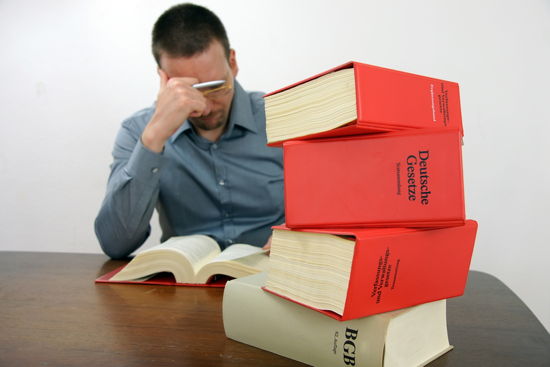 Student, der konzentriert ein Gesetzbuch liest, im Vordergrund weitere dicke Gesetzesbücher übereinandergestapelt