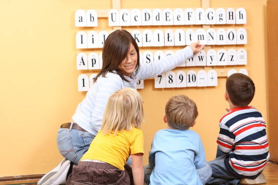 Erzieherin zeigt Kindern Buchstaben-Tafel