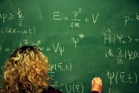 Grüne Tafel (von der Schreibenden ist nur der Kopf von hinten und die Hand zu sehen) beschrieben mit diversen Formeln