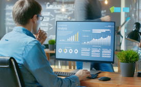 Junger Mann mit Brille schaut sich Statistiken auf einem Computerbildschirm an.