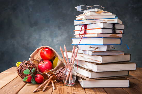 Stapel Bücher mit Markierungen, dazu einige Äpfel und Bleistifte