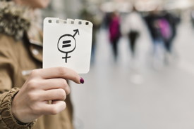 Frau hält ein Notizzettel mit den Geschlechtersymbolen und einem Gleichheitszeichen ins Bild