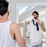 Ein Mann hält sich am Spiegel ein Hemd und eine Krawatte an - er macht sich für die Arbeit fertig