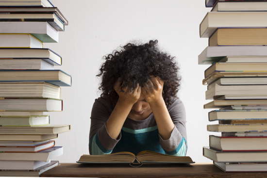 Studentin sitzt nachdenklich vor einem Buch, zwischen Bücherstapeln