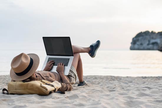 Frau am Strand mit Laptop und Sonnenhut