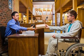 Student im Rollstuhl an der Bücherrückgabe der Bibliothek