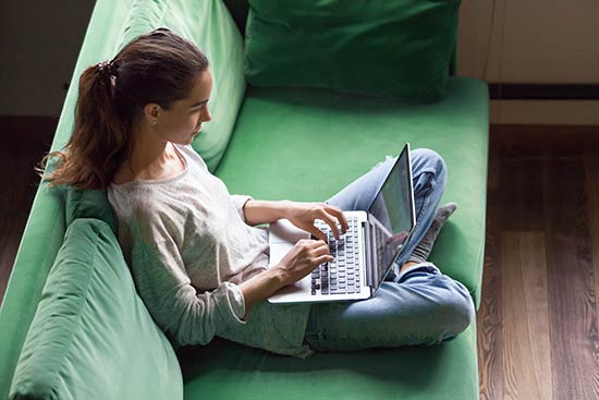 Studentin sitzt mit Laptop auf einer Couch